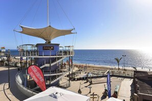 A seaside hotel with a central tower, a beach area with umbrellas, and a clear view of the ocean. - Holiday Home Meloneras Hills, Meloneras (San Bartolomé de Tirajana)