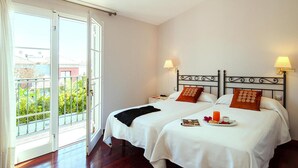 Une chambre d’hôtel avec deux lits, un balcon et un plateau de petit-déjeuner posé sur les lits.