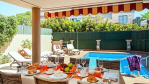 Un espace extérieur aménagé pour les repas, avec une piscine, des meubles en osier et une table dressée pour le petit-déjeuner.