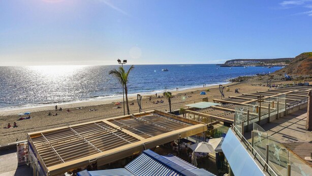 Un hôtel situé en bord de mer, doté d’espaces extérieurs aménagés pour s’asseoir, offrant une vue sur l’océan et sur une falaise éloignée.