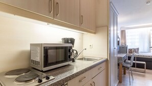A compact kitchen with a microwave, stove, and sink. There is a dining area with a table and chairs visible through an open door. - Ferienwohnung, St. Peter - Ording (St. Peter-Ording)