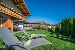 A hotel with a wooden facade, outdoor seating area with lounge chairs, and a well-maintained lawn. - Apartment in Brixen Near Wilder Kaiser Gondola (Brixen im Thale)