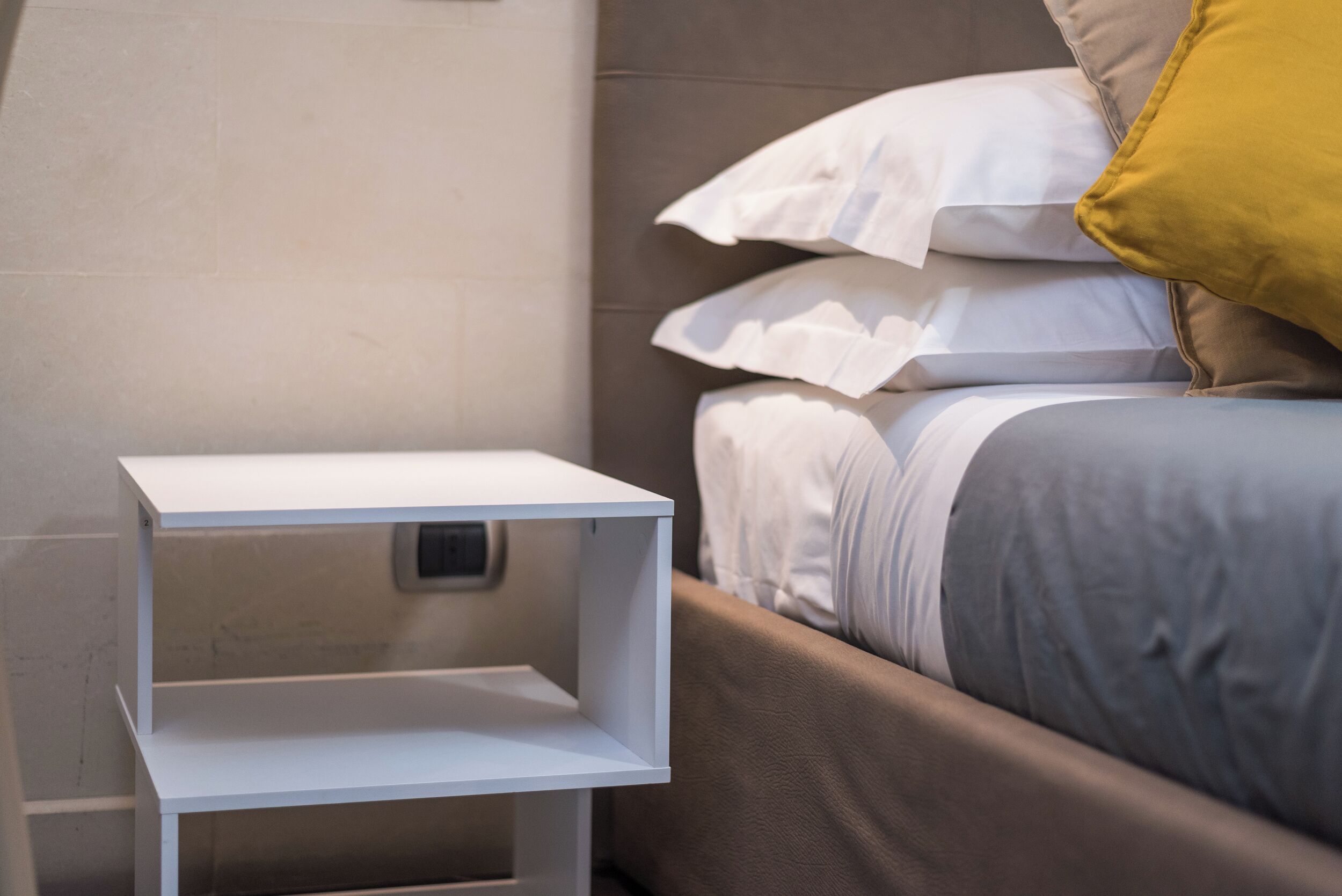 A neatly made bed with white and gray bedding, a brown headboard, and a yellow pillow.