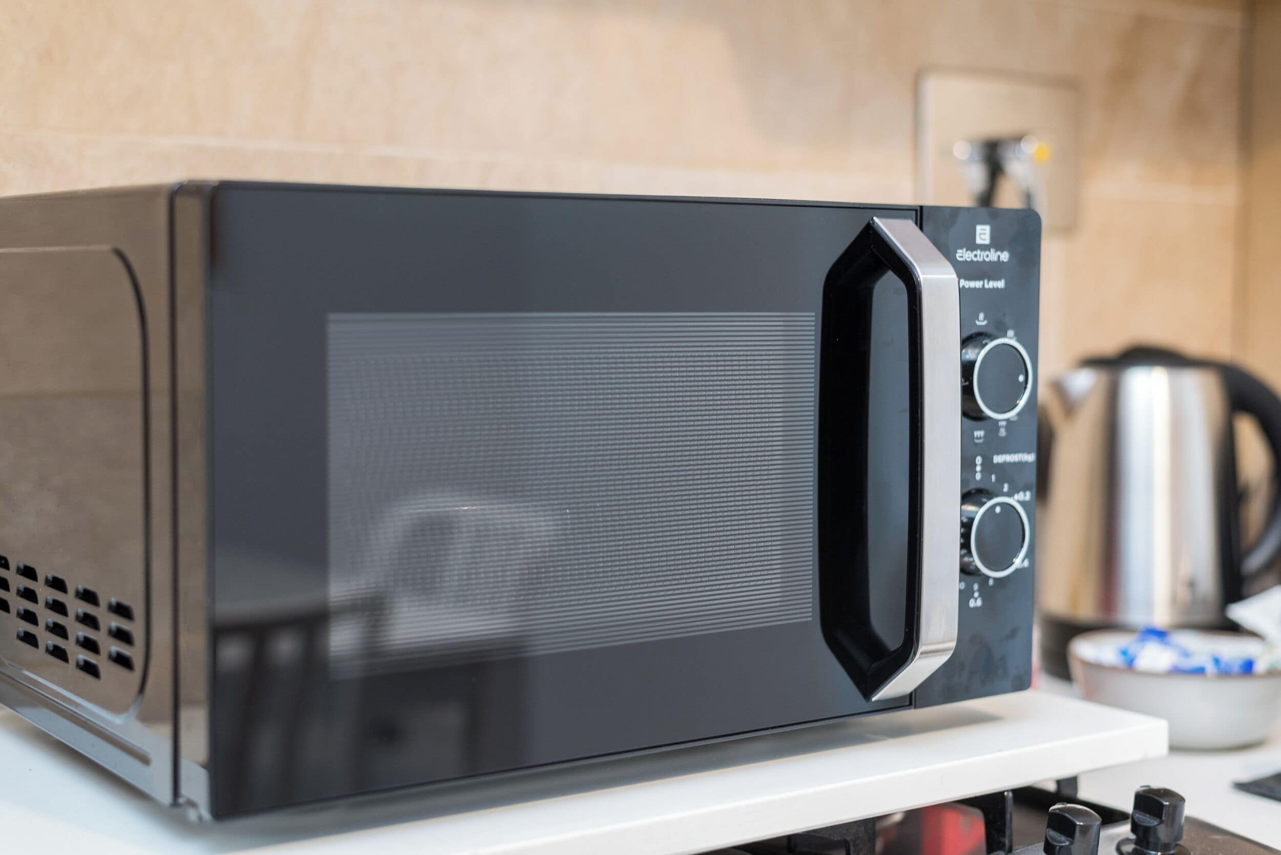 A black microwave oven with a digital display and control panel, placed on a white countertop in a kitchen setting.