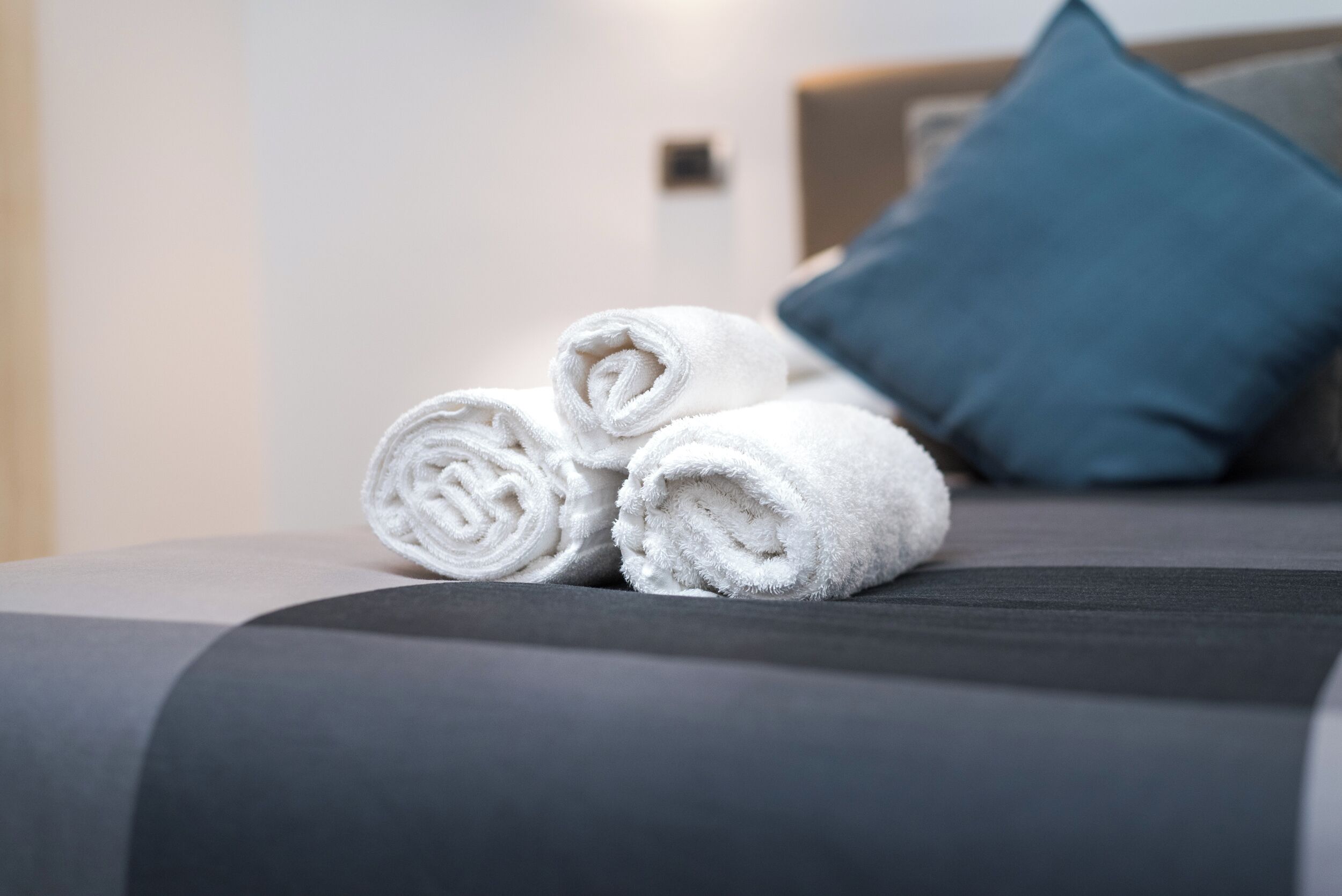 Ein ordentlich bezogenes Bett mit aufgerollten weißen Handtüchern und einem blauen Kissen.