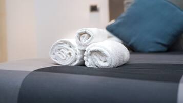 Ein ordentlich bezogenes Bett mit aufgerollten weißen Handtüchern und einem blauen Kissen.