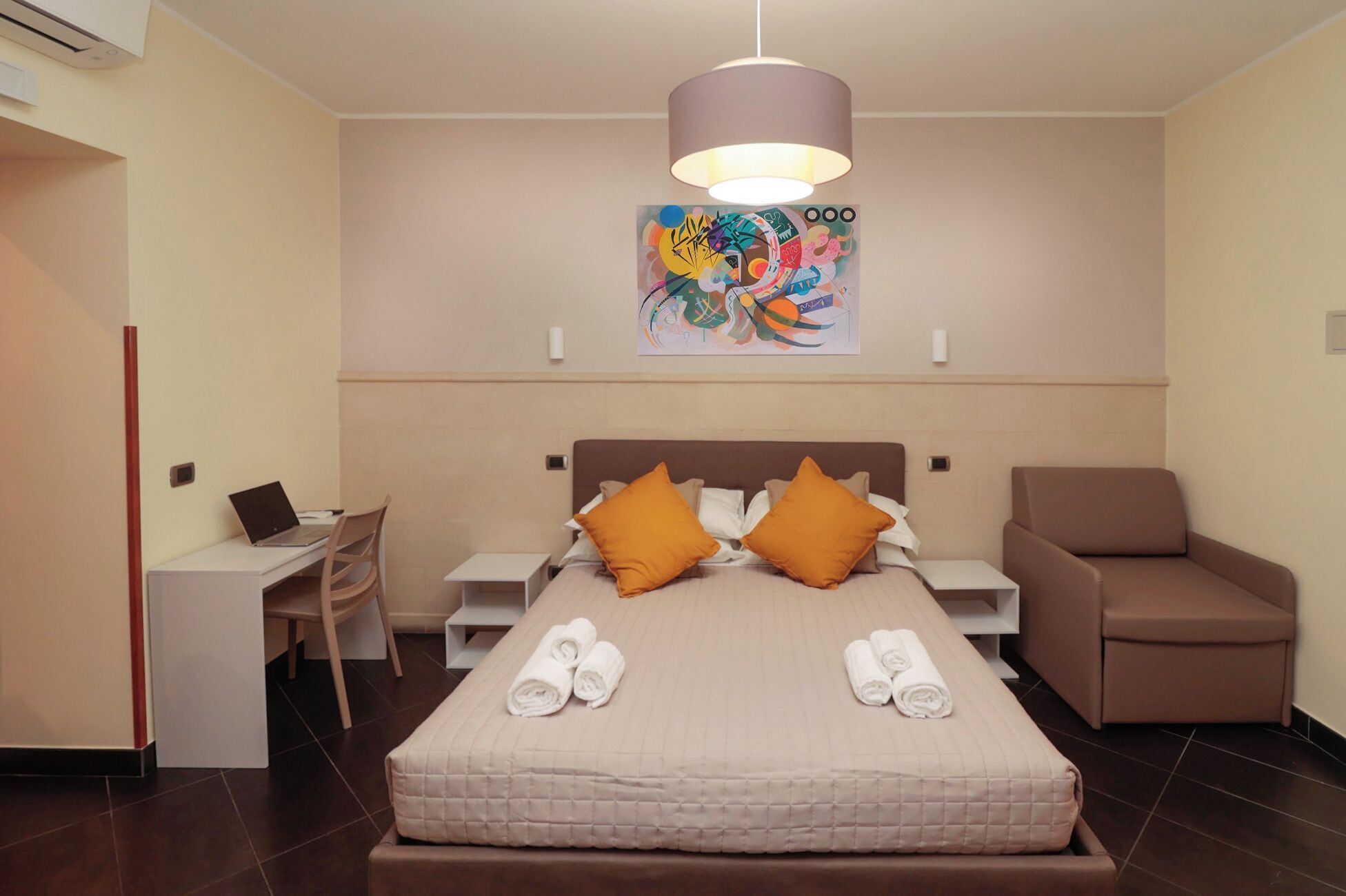 Ein Hotelzimmer mit einem Bett, zwei Kissen, einem Schreibtisch mit einem Laptop, einem Stuhl und einer Couch.