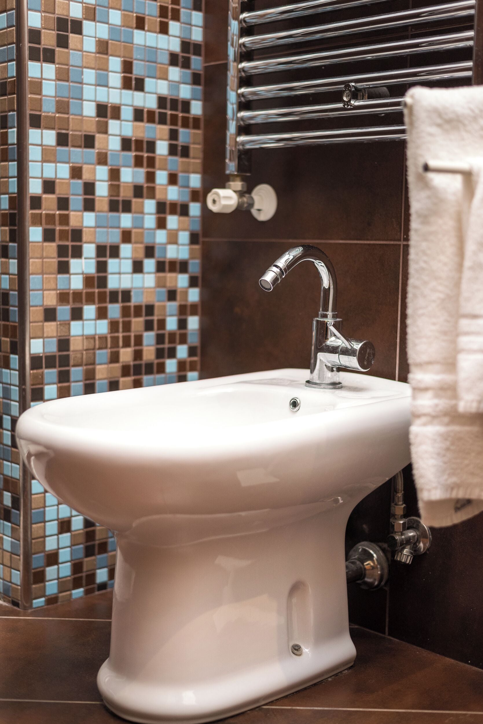 A bathroom with a white pedestal sink, chrome faucet, and a mosaic tile wall.