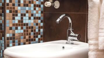 A bathroom with a white pedestal sink, chrome faucet, and a mosaic tile wall.