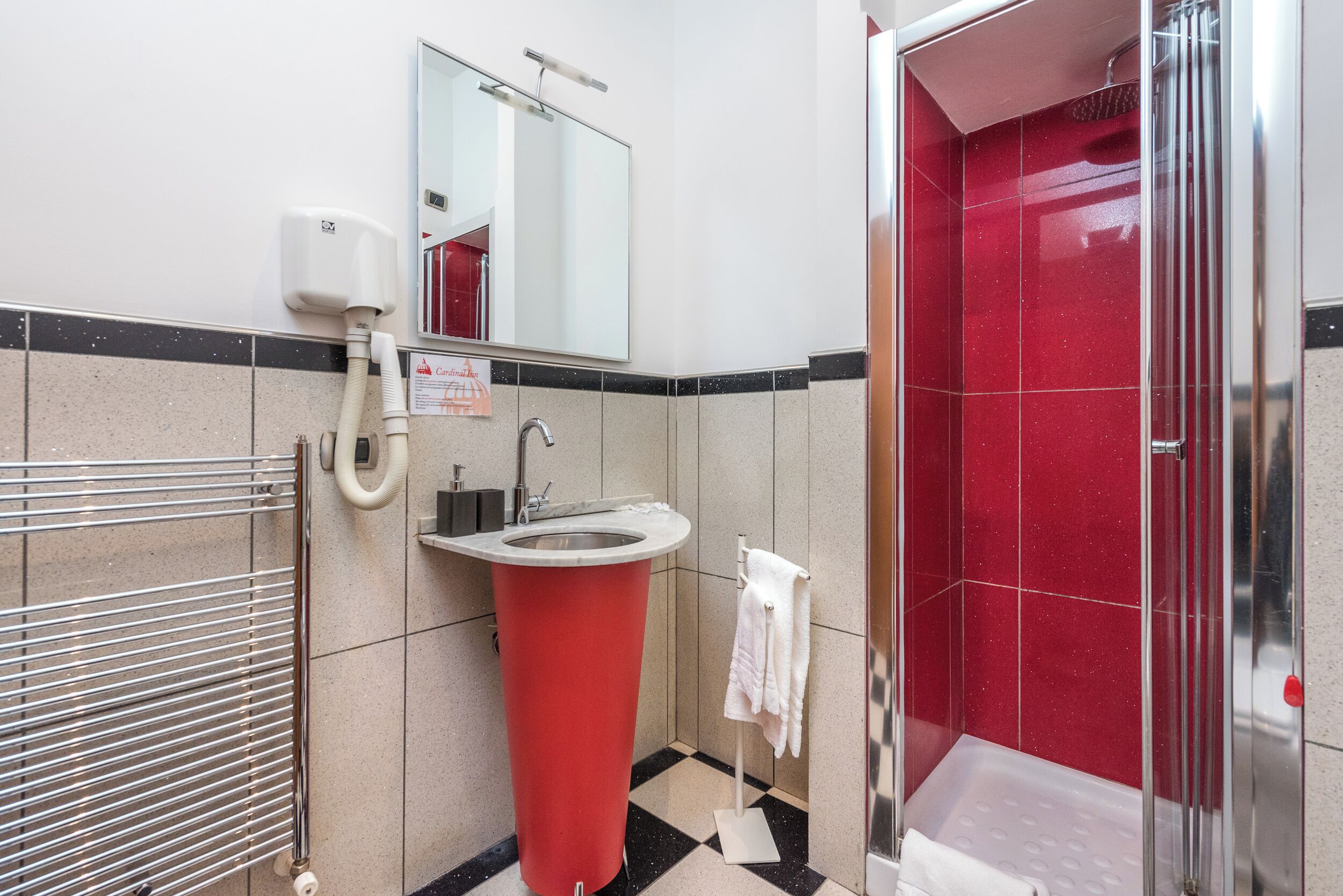 Een badkamer met een rode wastafel, een spiegel, een handdroger en een douchehoek.
