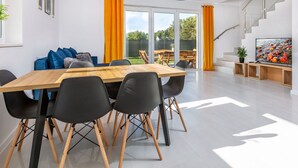 Un espace repas moderne avec une table en bois et des chaises noires, un escalier et un téléviseur posé sur un meuble en bois.