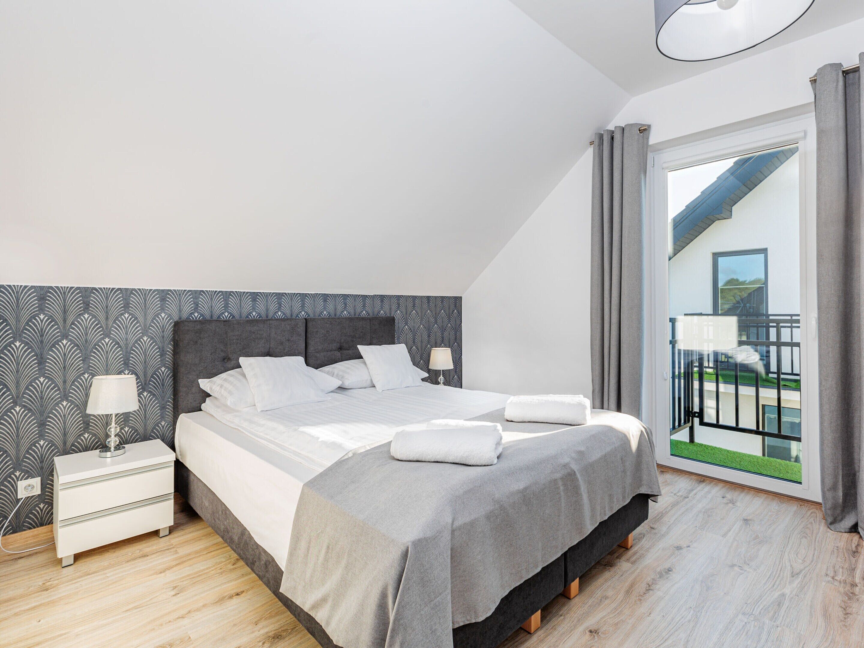 Un dormitorio moderno con una cama grande, una mesita de noche, una lámpara y vistas al balcón exterior.