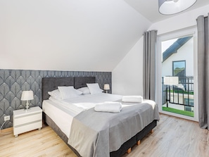 Ein modernes Schlafzimmer mit einem großen Bett, einem Nachttisch, einer Lampe und Blick auf den Balkon.
