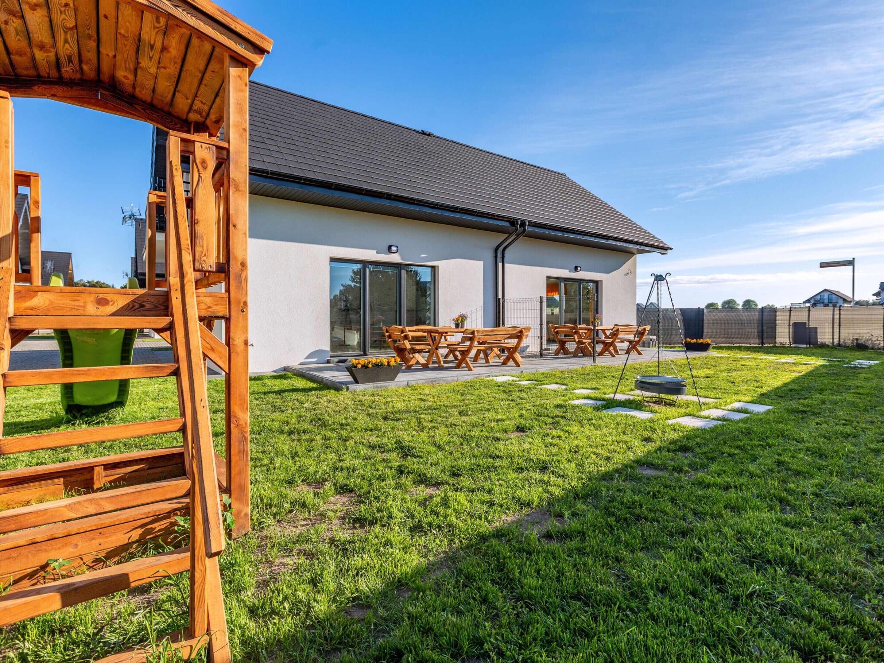 Una casa moderna con un patio, muebles de madera y un césped bien cuidado.