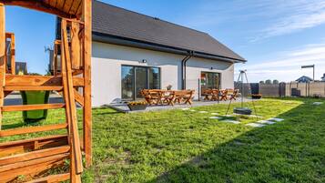 A modern house with a patio, wooden furniture, and a well-maintained lawn.