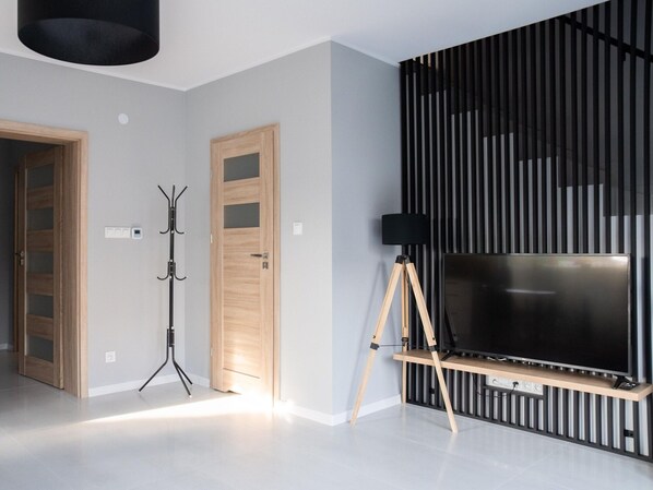 A modern living room with a large flat-screen TV on a wooden stand, a tripod, and a coat rack.