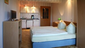 Una habitación de hotel compacta con cama, una kitchenette pequeña, un televisor y una puerta de madera.