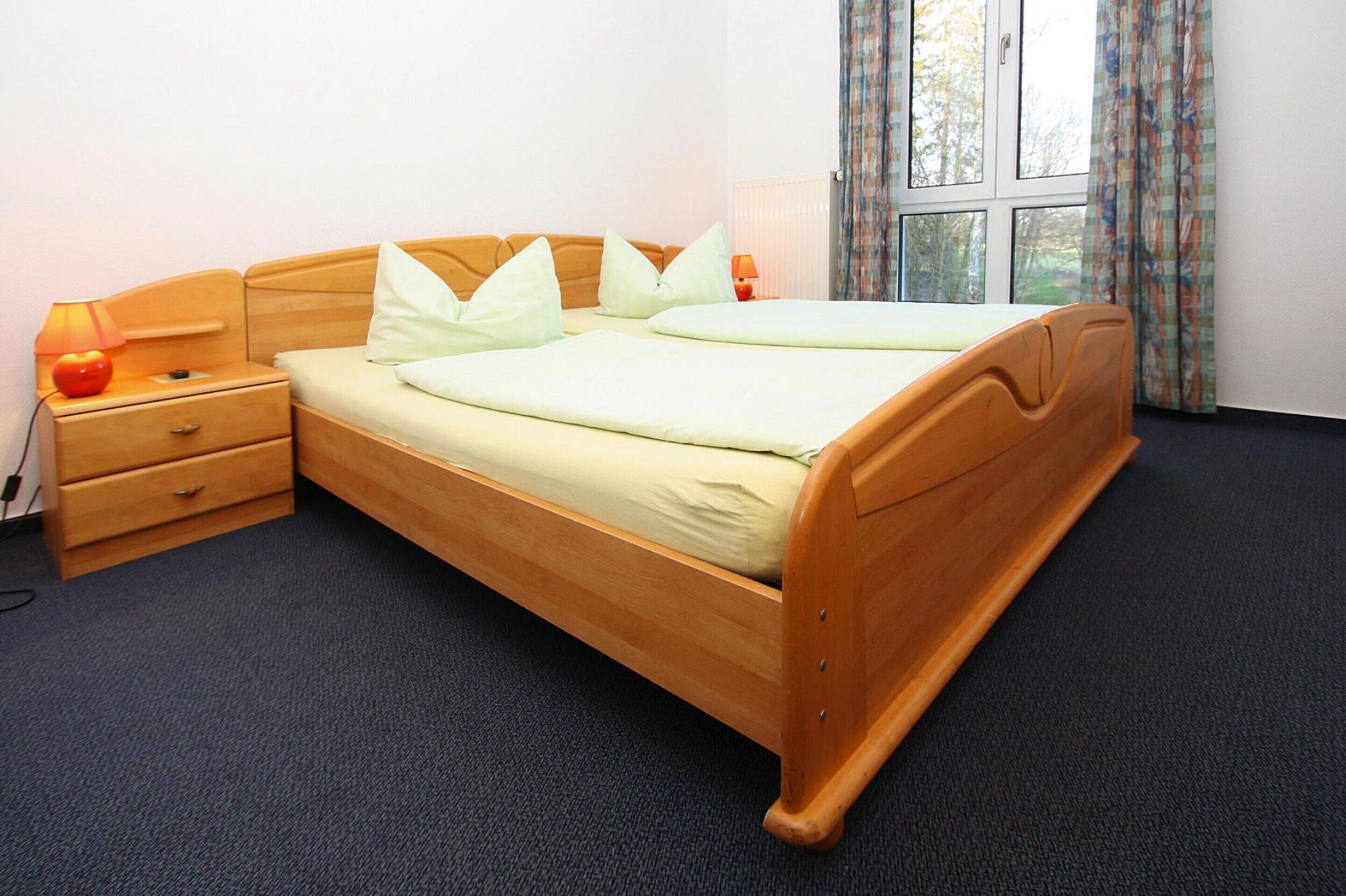 A double bed with a wooden frame, two pillows, a bedside table with a lamp, and a window with curtains.