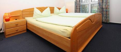 A double bed with a wooden frame, two pillows, a bedside table with a lamp, and a window with curtains.