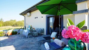 Une terrasse extérieure avec un espace repas, des chaises longues et un parasol vert.