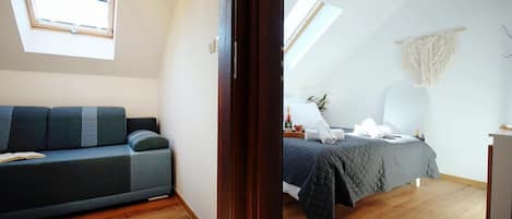 A modern bedroom with a dark-colored sofa, a bed with a quilted bedspread, and a small bedside table.