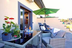 Une terrasse avec des meubles en osier, une table en verre et un parasol vert.