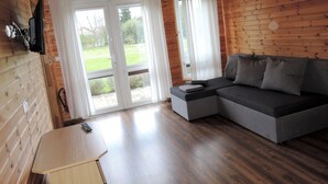 A wooden cabin interior with a sofa, a small table, and a TV mounted on the wall. - Holiday Houses for 4 People in Rewal-formerly TUI Ferienhaus (Rewal)