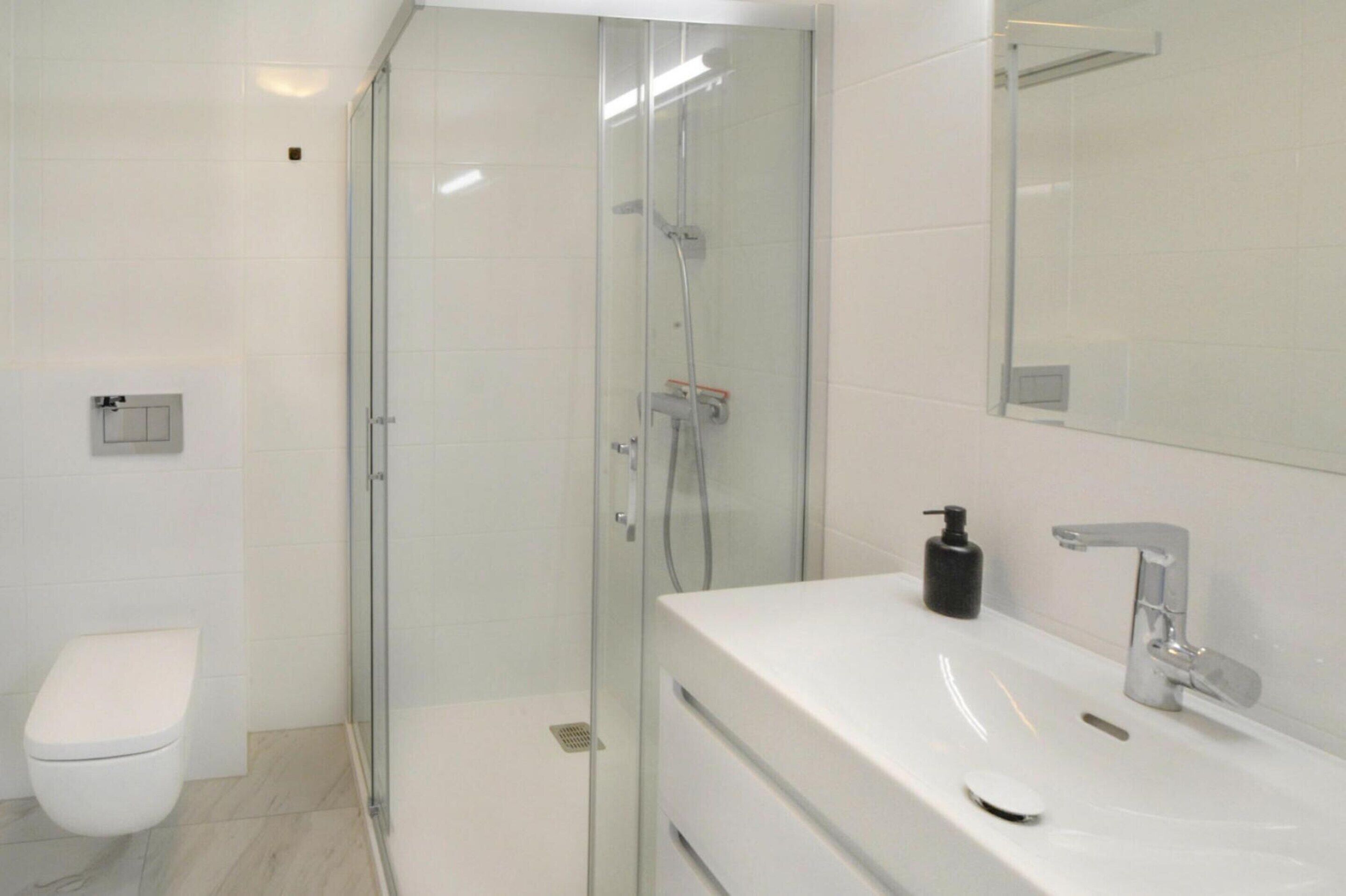 A modern bathroom with a glass-enclosed shower, a white toilet, and a vanity with a mirror and sink.
