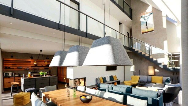 A spacious living area with a wooden dining table, grey upholstered sofas, and a staircase leading to an upper level. - Exklusives Landhaus auf Fehmarn (Fehmarn)