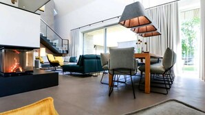 A modern living room with a fireplace, comfortable seating, and a dining area. - Exklusives Landhaus auf Fehmarn (Fehmarn)
