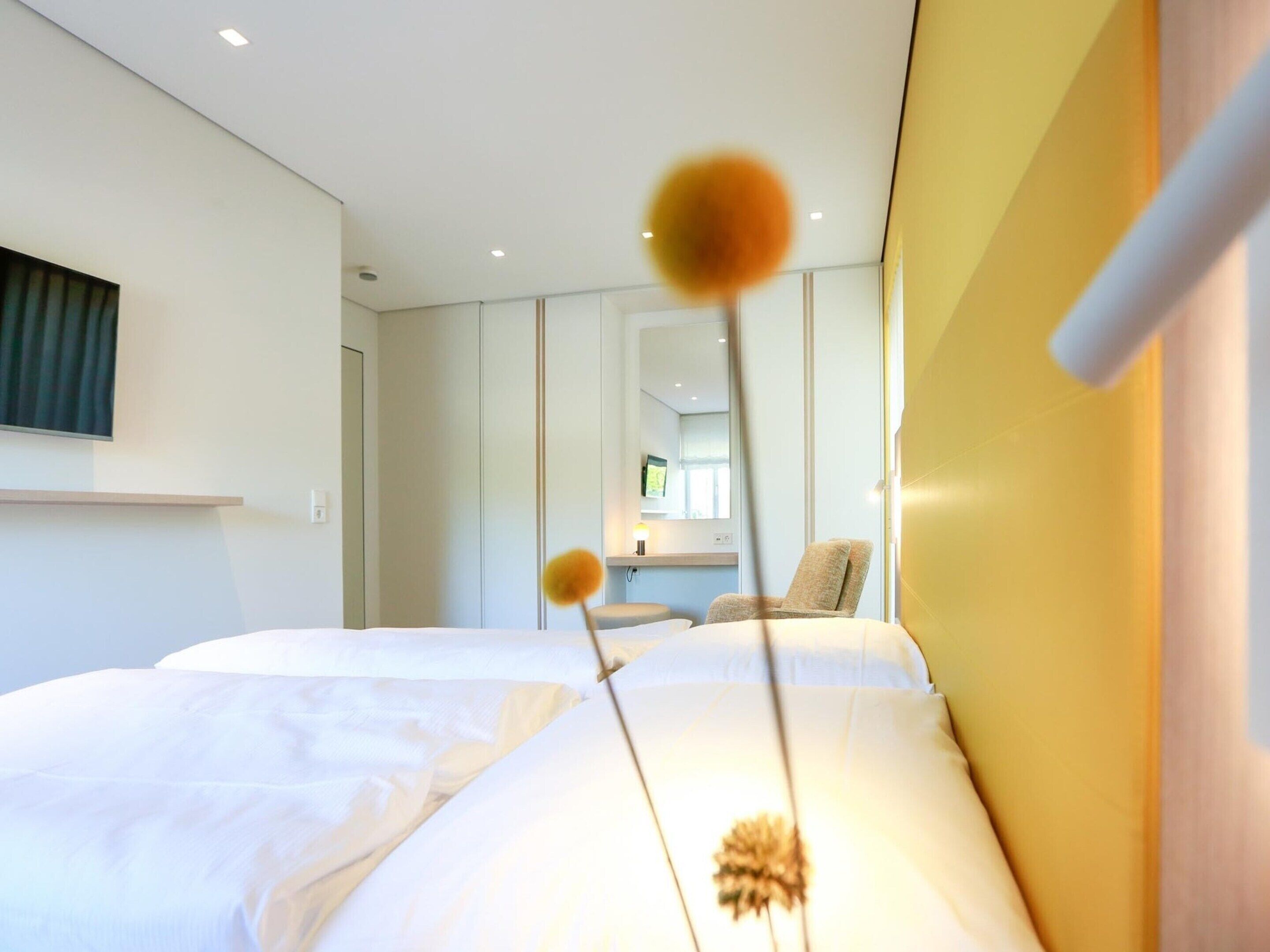 Een moderne hotelkamer met twee bedden, een grote spiegel en een gele accentmuur.