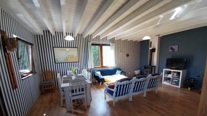 Ein Zimmer mit gestreifter Wandgestaltung, einem Esstisch mit Stühlen, einem blauen Sofa, einem Fernseher und einem Kamin.