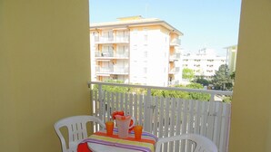A balcony with a table and chairs, a white fence, and a view of apartment buildings in the background. - Apartment in Bibione With Balcony (San Michele al Tagliamento)