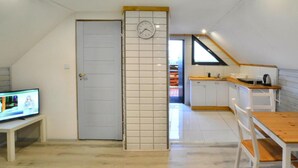A compact kitchen with a wooden table and chairs, a clock on the wall, and a television on a stand. - Apartment in Jezierzany Near Lake Wicko (Postomino)