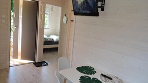 Ein Zimmer mit einem Bett, einem an der Wand montierten Fernseher, einem Tisch mit Unterlage und einer Tür zu einem anderen Raum.
