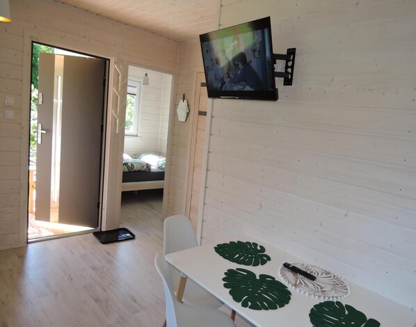 Une pièce comprenant un lit, un téléviseur fixé au mur, une table avec un set de table et une porte donnant sur une autre pièce.
