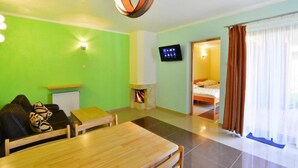 A room with a green wall, a fireplace, a TV, a bed, and a dining area. - Spacious Holiday Home With Private Garden (Mielno)