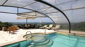 Une piscine à débordement entourée de parois en verre, dotée de chaises longues et de parasols, et offrant une vue sur le paysage.