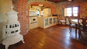 Une cuisine rustique avec un mur en pierre, des poutres en bois et un coin repas comprenant une table et des chaises.