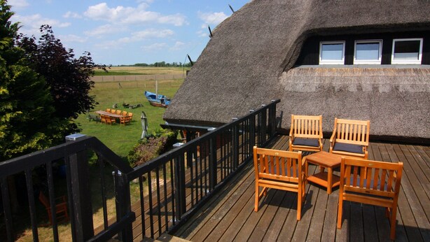 A thatched-roof building with a wooden deck, outdoor seating, and a view of the surrounding landscape. - Ferienwohnung Strandanker in Monkebude (Monkebude)