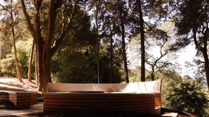A bench with a brick base and a white cushion, surrounded by trees in a park setting.