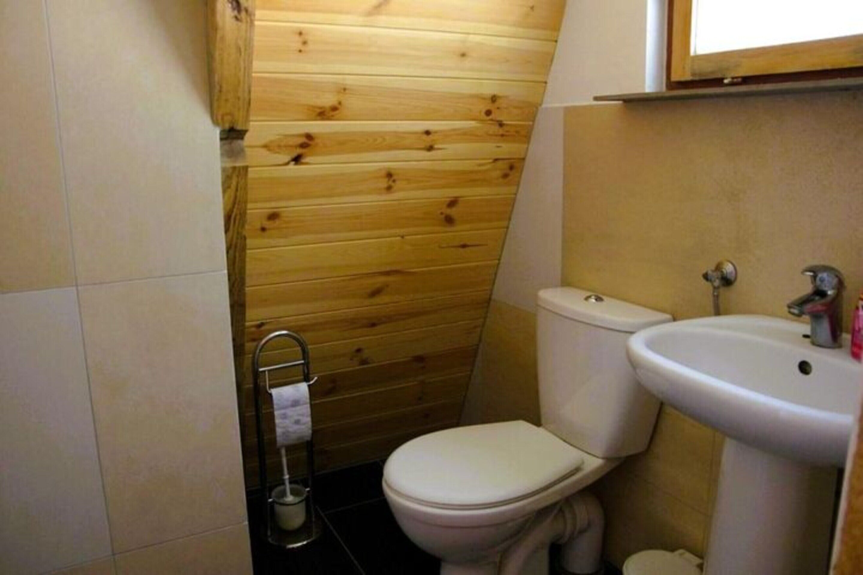 A small, compact bathroom with a wooden wall, a white toilet, and a white sink.