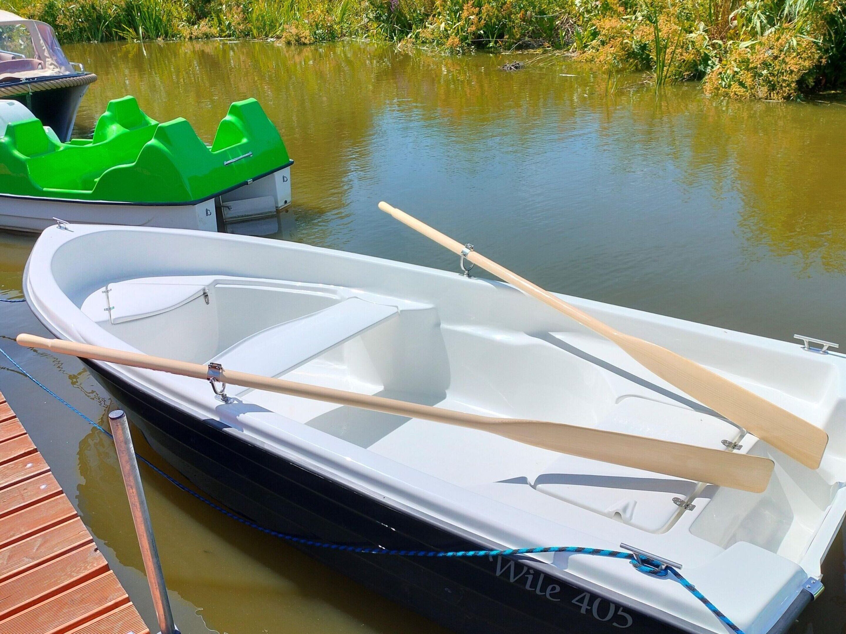 Une petite barque blanche à rames, avec deux rames en bois et une corde bleue attachée au quai.