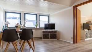 Una sala de estar moderna con comedor, ventanas amplias, un televisor de pantalla plana y piso de madera.