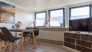 Una habitación moderna con comedor, televisor y ventanas amplias.