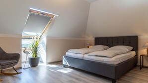 Un dormitorio moderno con una cama grande, una silla, una planta y un tragaluz.