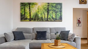 A living room with a grey sectional sofa, a wooden coffee table, and a forest-themed painting on the wall.