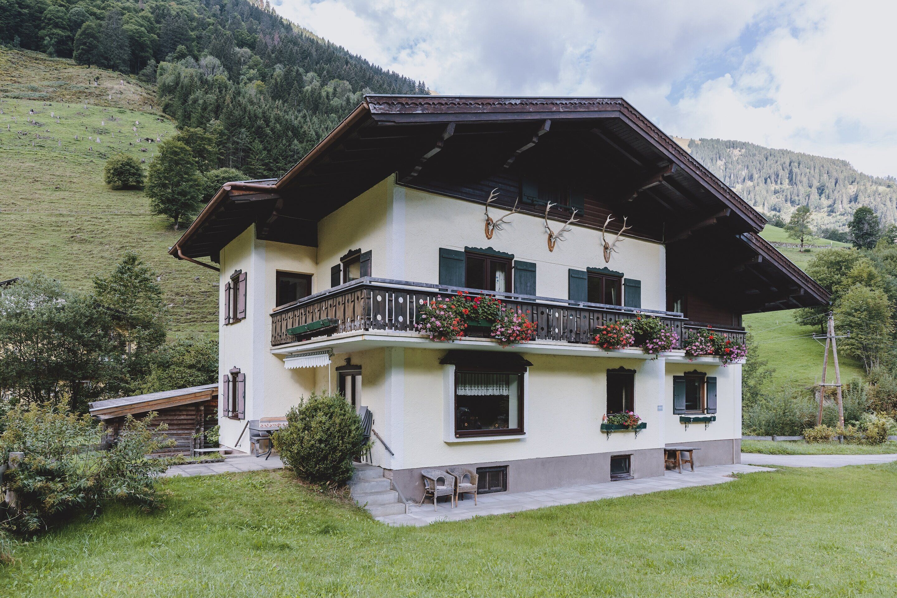 Un chalet de dos plantas con balcón, escalera de madera y jardín.