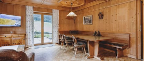 Un interior de madera con comedor, un televisor en la pared y vistas a través de la puerta de vidrio.