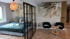 Una camera da letto moderna con un letto, una parete divisoria in vetro, un murale e due sedie.